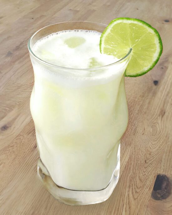 Glas mit brasilianischer Limonade, gefüllt mit einer heller, sprudelnder Flüssigkeit und einer Limettenscheibe als Garnitur.