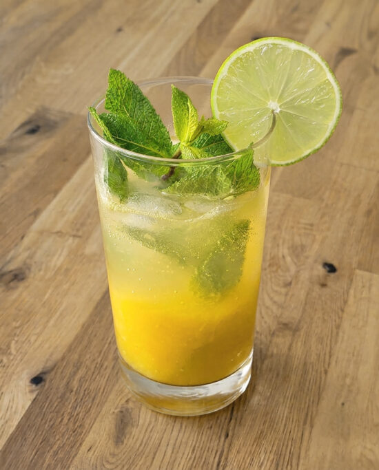 Fruchtiger Mango Mojito mit frischer Mango, Limette, Minze und weissem Rum im Glas auf einem Holztisch