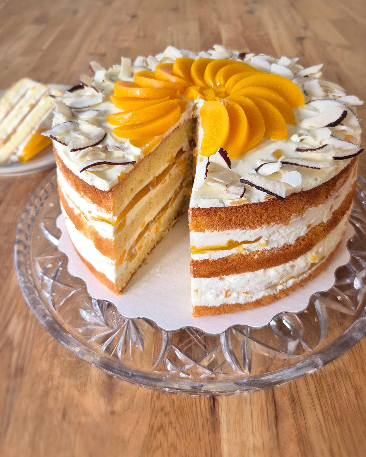 Pfirsich-Maracuja-Quarktorte mit Kokos, mehrere Biskuitlagen, Quarkcreme mit Pfirsichstückchen und Maracujaspiegel, Garnierung aus Kokoschips und Pfirsichspalten.