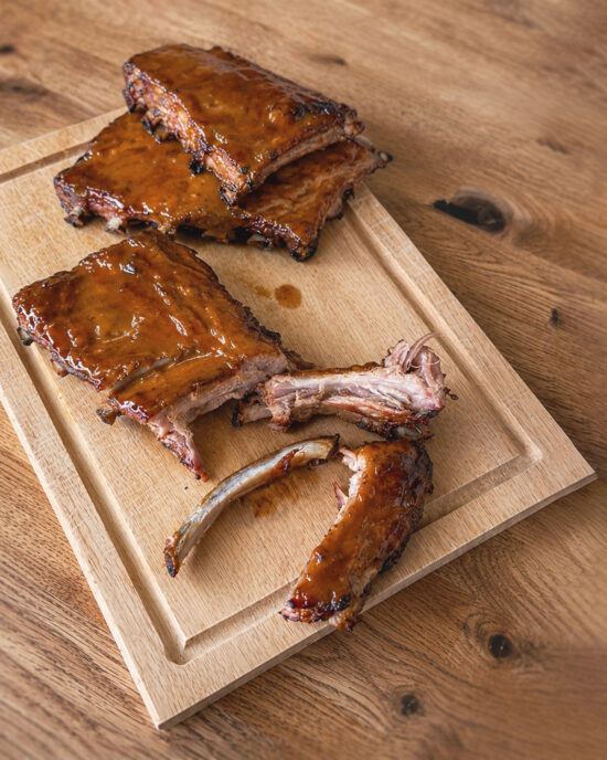 Saftige Spareribs mit Honig-Senf-Glasur liegen in Stücken auf einem Holzbrett und zeigen das zarte Fleisch, das sich perfekt vom Knochen löst.