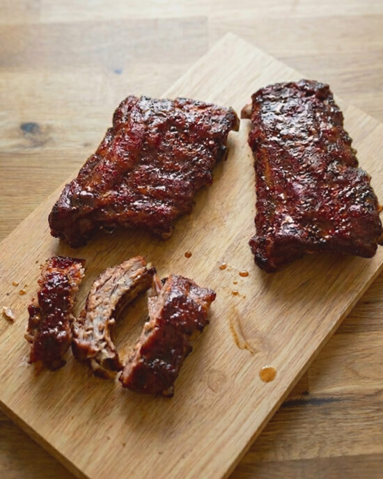Zarte Spareribs mit Ahornsirup-Whiskey-Glasur liegen auf dem Schneidebrett, daneben ein aufgeschnittener Rack mit glänzender BBQ-Kruste.