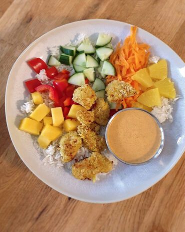 Sommerliche Hähnchen-Bowl mit knusprig paniertem Hähnchen, buntem Gemüse, Basmati-Reis und cremiger Erdnuss-Sauce in einer Schüssel mit Ananas und Mango.