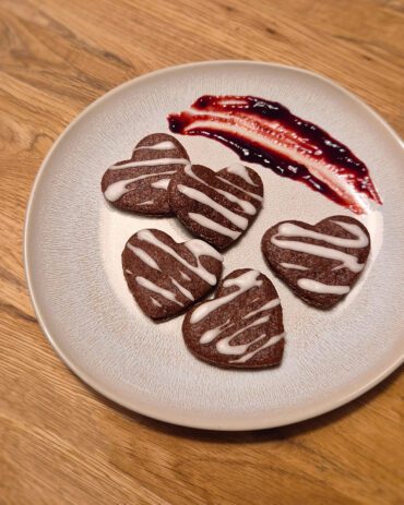 Schwarzwälder Kirschplätzchen in Herzform, angerichtet auf einem hellen Teller mit Sauerkirschkonfitüre dekoriert