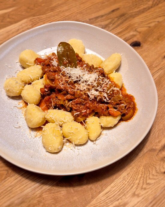 Kartoffel-Gnocchi mit Bolognese, garniert mit Lorbeerblatt und geriebenem Parmesankäse