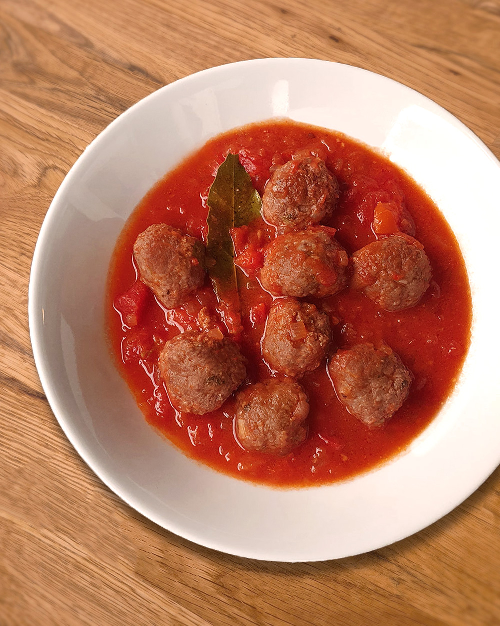 Eine Schüssel mit Albóndigas, Fleischbällchen in Tomatensauce, garniert mit einem Lorbeerblatt.