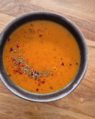 Schüssel mit türkischer orangefarbener Linsensuppe, die mit Pul Biber und getrockneter Minze garniert ist.