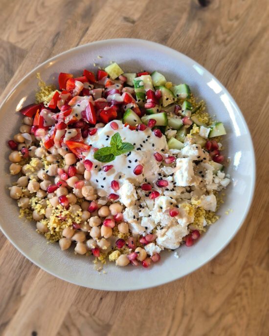 Orientalische Couscous Bowl mit Feta und Tahini Sauce: cremiger Joghurt, körniger Couscous, rote Paprika, Gurken, Kichererbsen, Granatapfelkerne mit Joghurt und Minze.