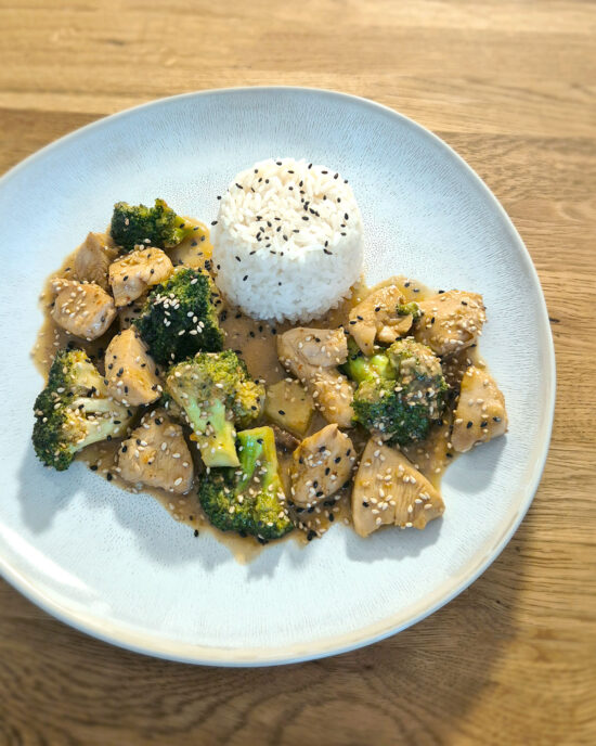 Hähnchen und Brokkoli in Honig-Sesam-Sauce mit Jasminreis auf hellem Teller, glänzende goldbraune Sauce, grüne Brokkoliröschen und Sesam über dem Gericht