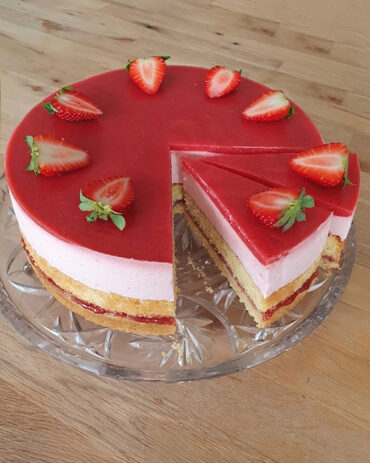 Runde Erdbeertorte mit sichtbaren Schichten aus Mürbeteig, Biskuit, heller Erdbeercreme und rotem Erdbeerspiegel, garniert mit halbierten frischen Erdbeeren