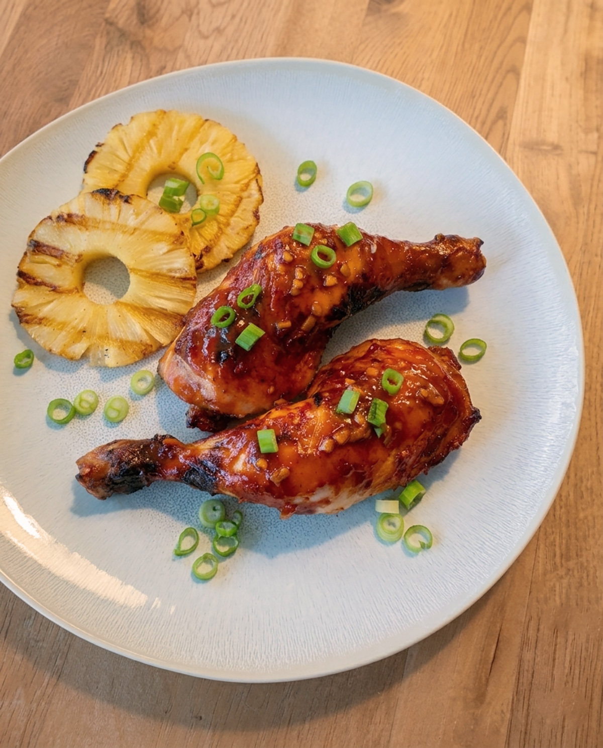 Karamellisiertes Huli Huli Chicken vom Grill mit Ananas, würzig-süsser Marinade und frischen Frühlingszwiebeln auf einem weissen Teller.