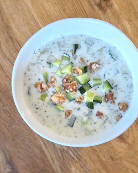 In einer weißen Schale wird Tarator serviert, eine bulgarische kalte Gurkensuppe mit Joghurt, Gurkenwürfeln, Dill und Walnüssen.