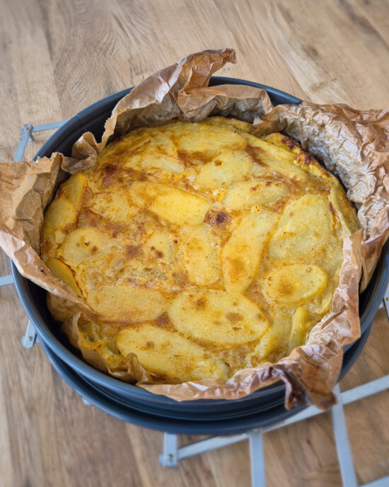 Eine goldbraun gebackene Ofen-Tortilla mit Kartoffelscheiben liegt in einer mit Backpapier ausgelegten Springform und zeigt die spanische Tortilla de Patatas.