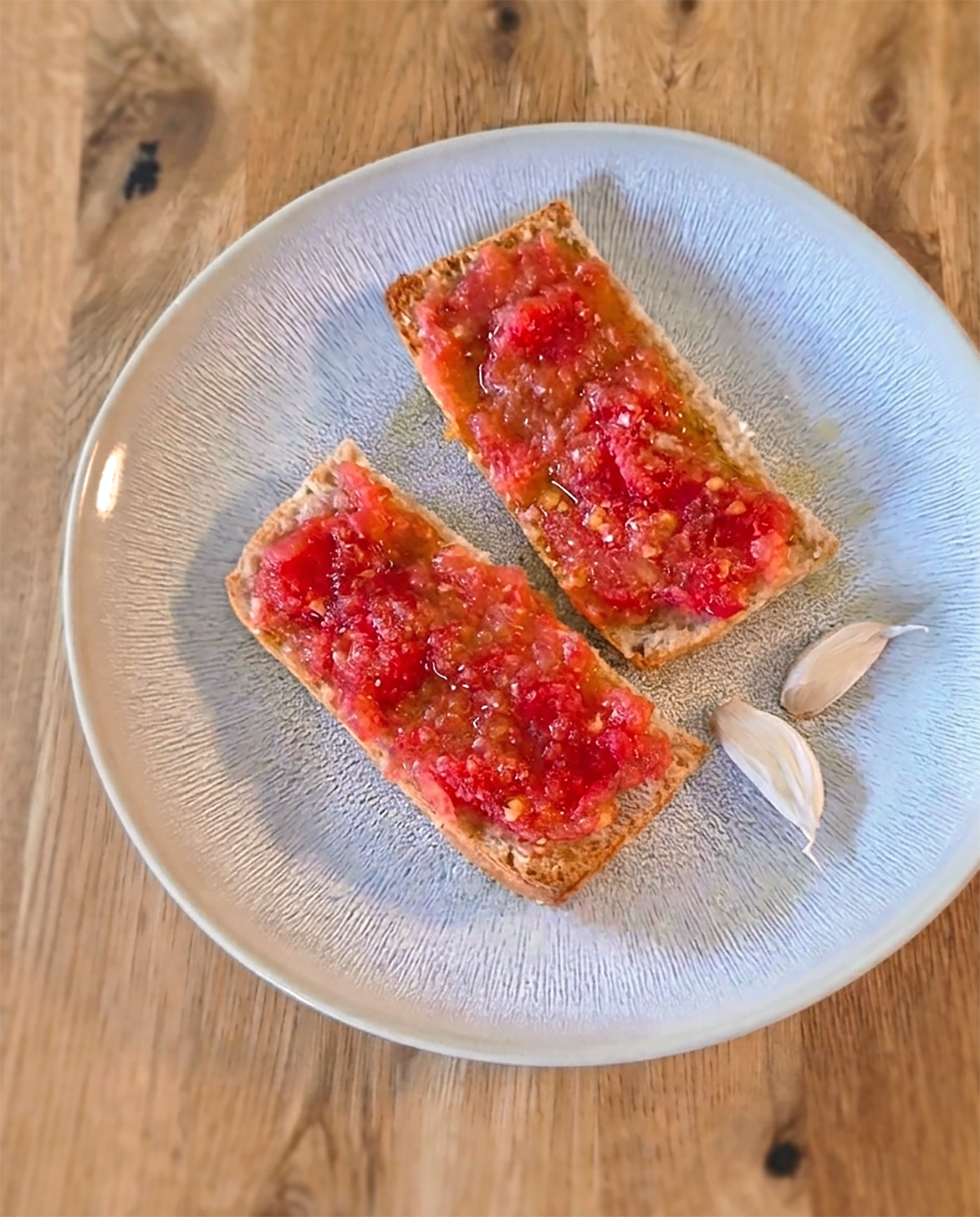 Auf dem Teller liegen zwei Stücke Pan con tomate mit geriebenen Tomaten, Knoblauch und Olivenöl auf knusprigem Brot - nach spanischer Art.