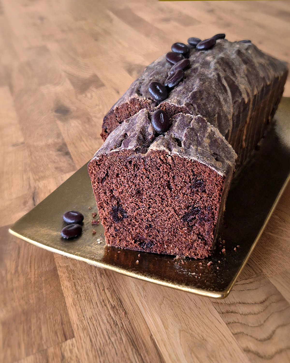 Ein saftiger Schokoladen-Kaffeekuchen mit Espressoglasur und Schokostückchen, als Cake gebacken, auf goldener Platte serviert und ein Stück abgeschnitten