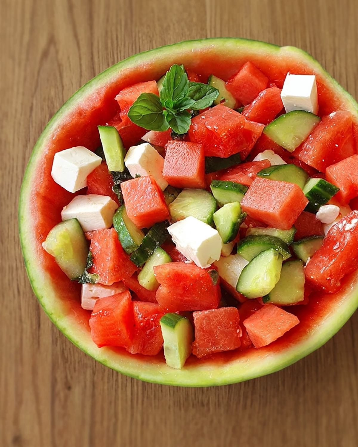In einer ausgehöhlten Wassermelonenhälfte wir ein sommerlicher Wassermelonen-Gurken-Salat mit Feta und frischer Minze serviert.