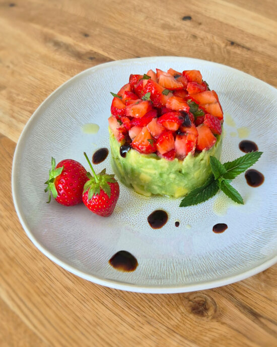 Ein Erdbeer-Avocado-Tatar mit gewürfelten Erdbeeren, cremiger Avocado, Minze und Balsamicocreme, angerichtet auf einem Teller mit frischen Erdbeeren.