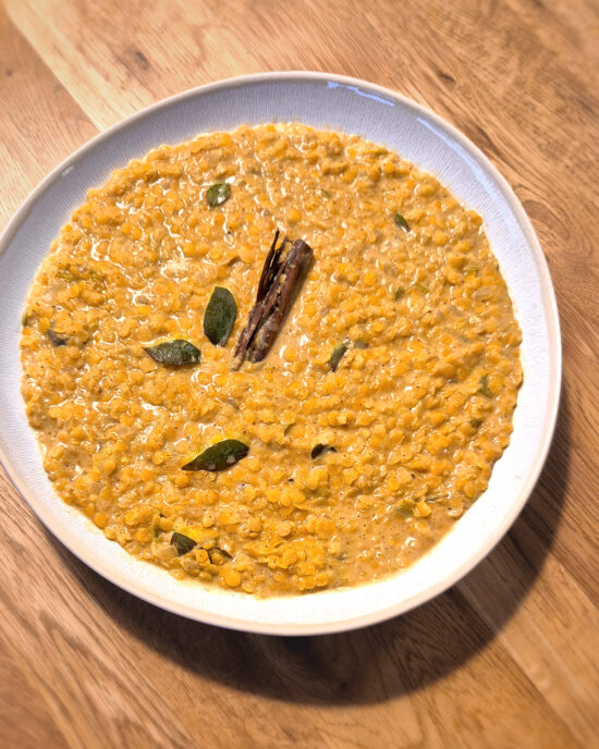 Gelbliches Sri Lanka Linsencurry, Parippu genannt, aus roten Linsen mit Curryblättern und Zimtstange in einer weißen Schüssel.
