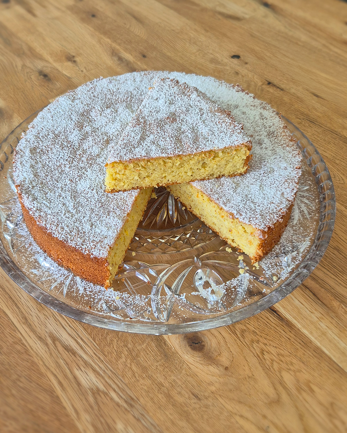 Aufgeschnittenes Stück Mallorquinischer Mandelkuchen mit Puderzucker auf einer Glasplatte, saftig und aromatisch.