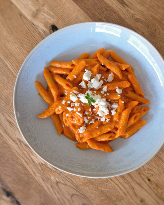 Cremige Paprika-Feta-Pasta mit gerösteter Spitzpaprika-Sauce, Penne und zerbröseltem Feta auf einem hellen Teller