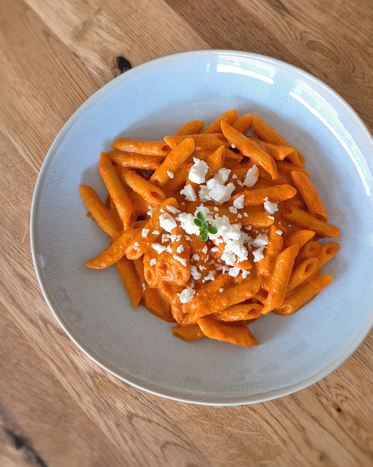 Cremige Paprika-Feta-Pasta mit gerösteter Spitzpaprika-Sauce, Penne und zerbröseltem Feta auf einem hellen Teller