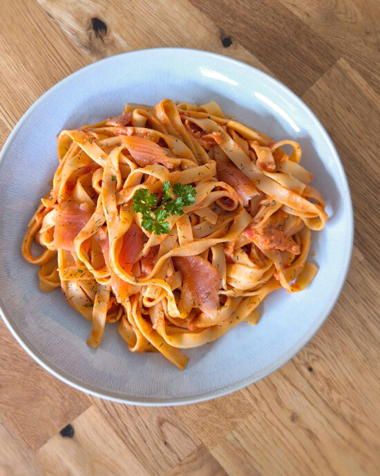 Cremige Tagliatelle al Salmone mit zartem Räucherlachs, Tomaten-Sahnesauce und frischer Petersilie auf einem Teller.