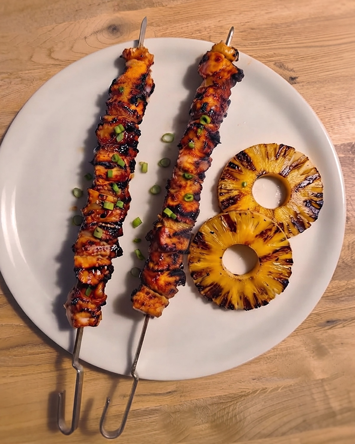 Gegrillte Huli-Huli-Hähnchenspiesse mit Ananas und karamellisierter Glasur liegen neben goldbraun gegrillten Ananasscheiben.