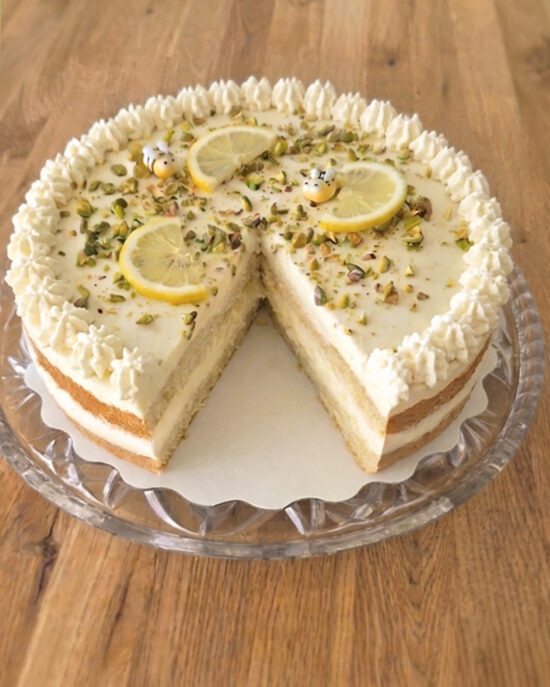 Erfrischende Zitronentorte mit Buttermilchcreme, Pistazien und Zitronenscheiben, angeschnitten auf einer Glasplatte serviert.
